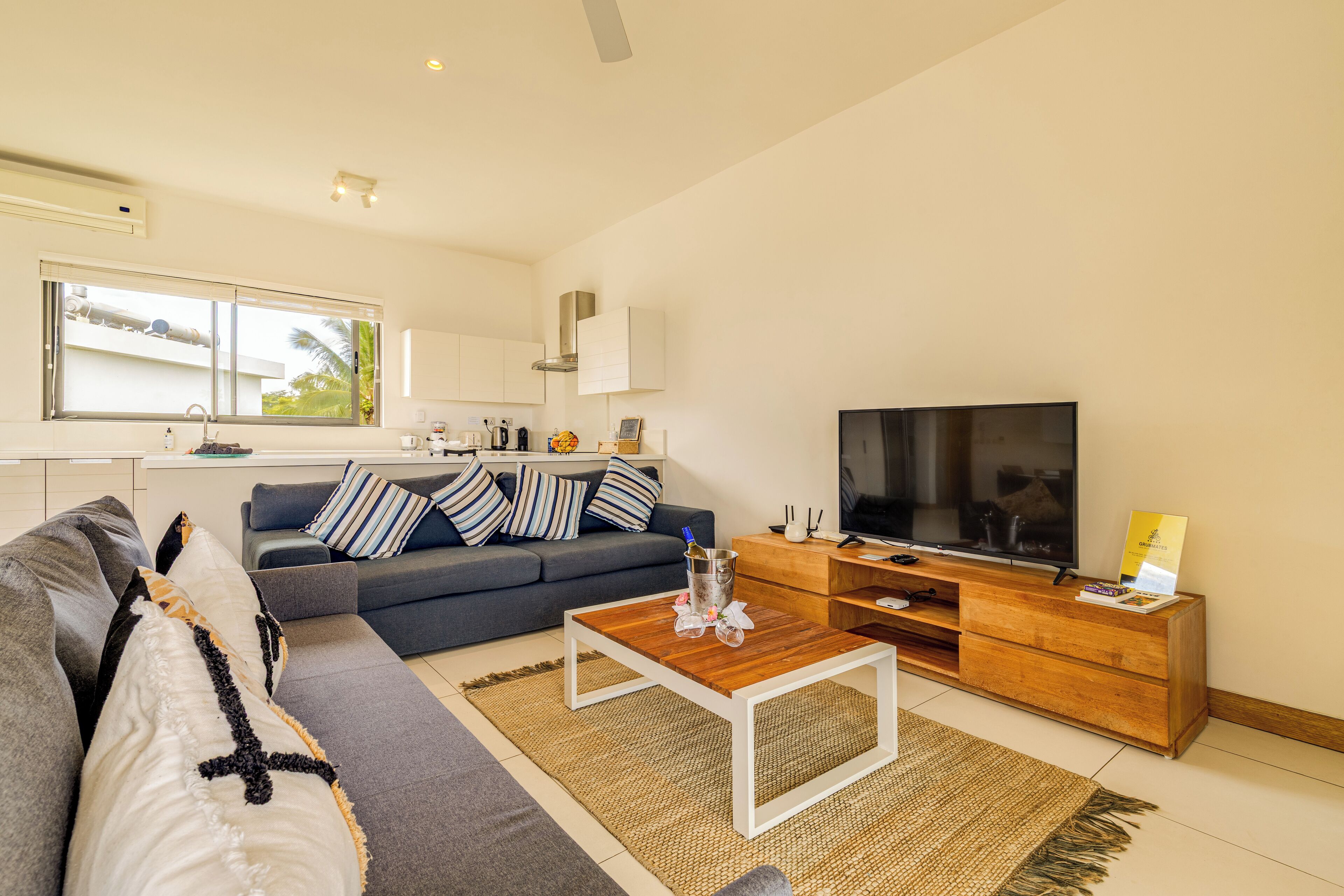 A modern living room with a grey sofa, a coffee table, a TV, and a kitchen area in the background.