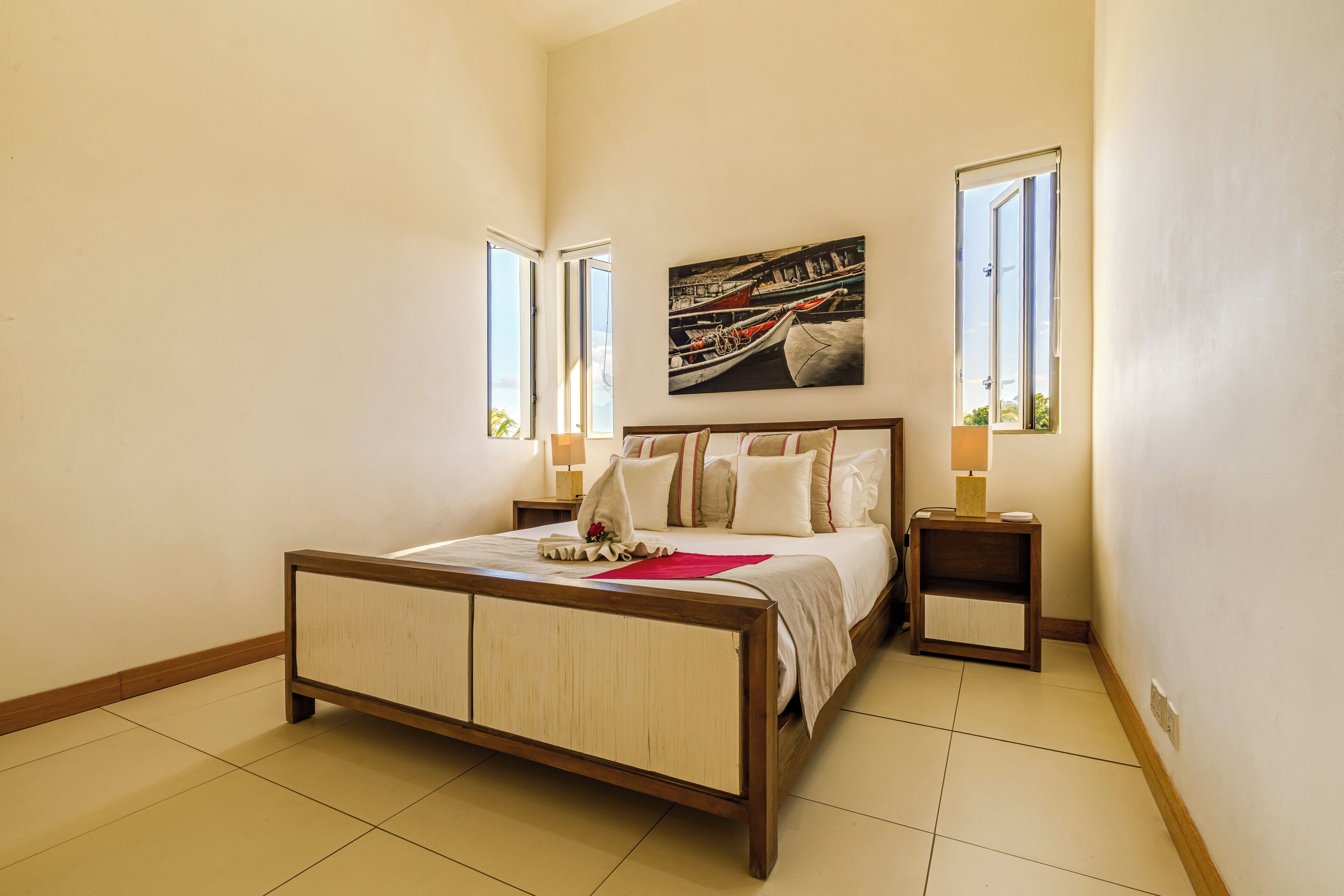 A bedroom with a wooden bed, two bedside tables, a nightstand, a window, and a painting on the wall.