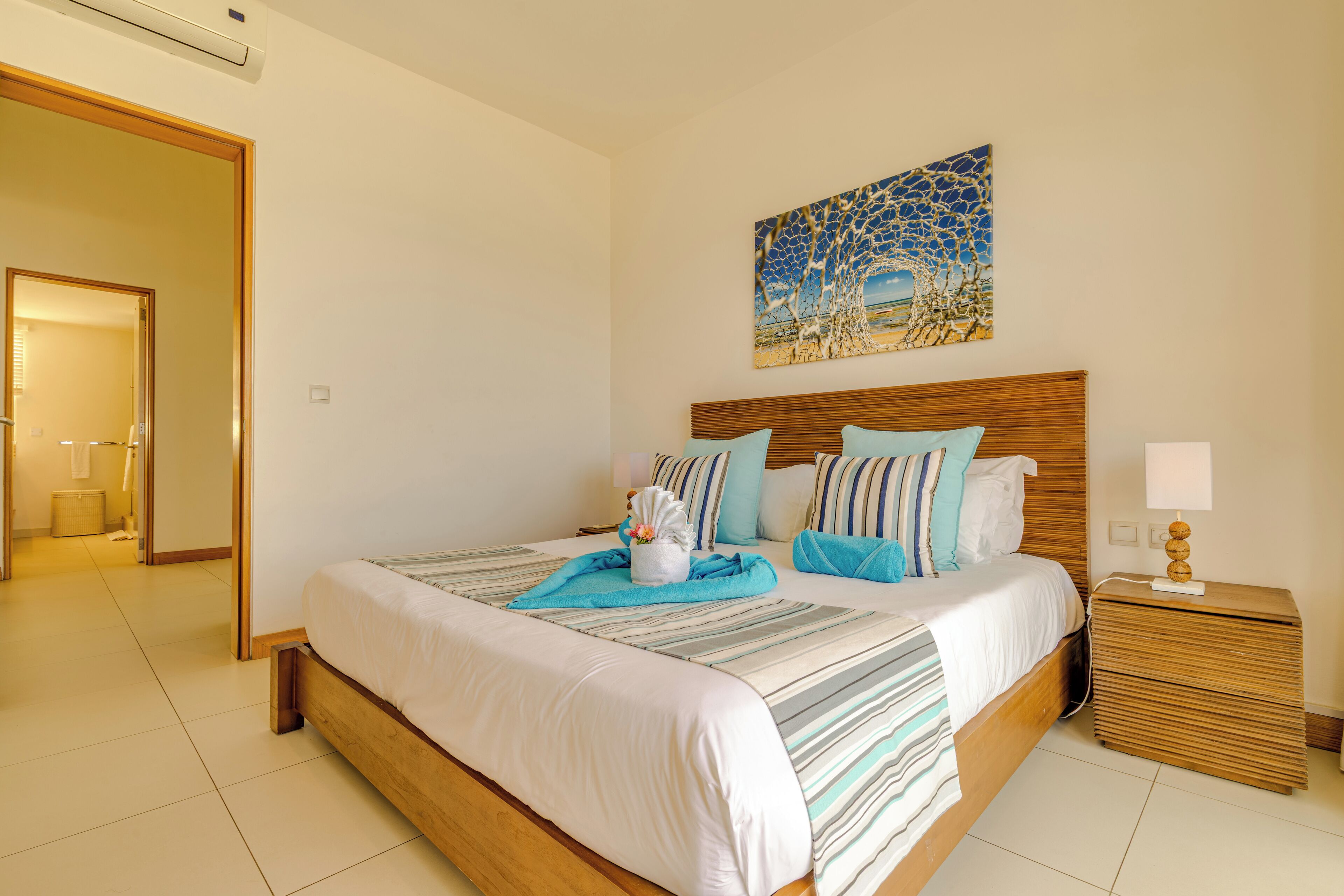 Una habitación de hotel ordenada con una cama grande, un cabecero de madera y una mesita de noche con lámpara.