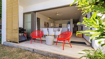 An open-plan living area with a dining table and red chairs, a kitchen in the background, and a sliding glass door leading to a balcony.