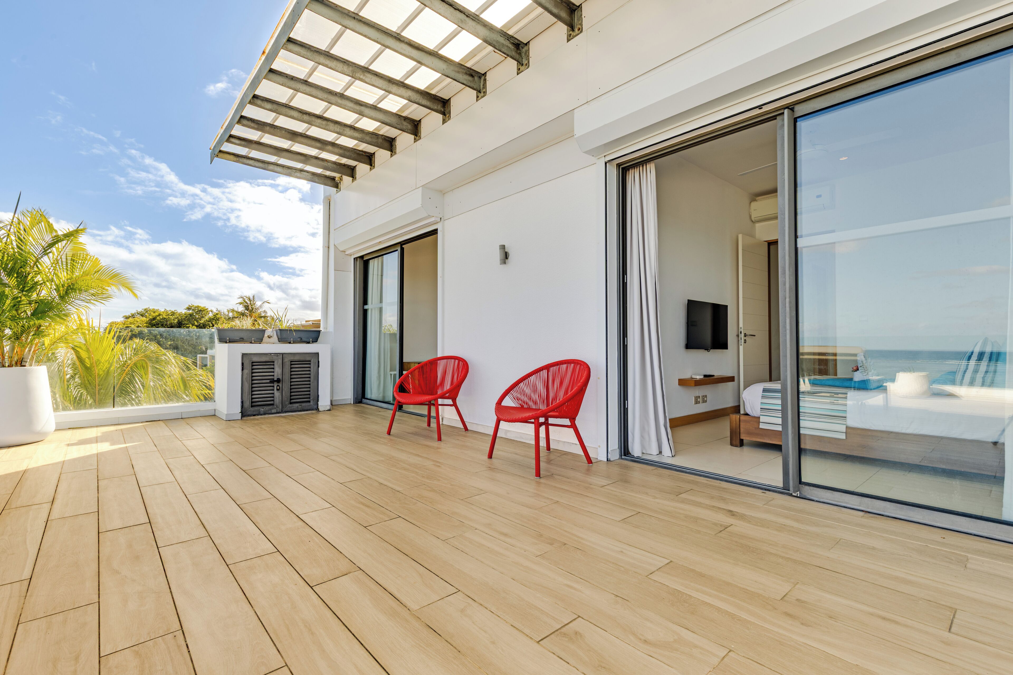 A modern room with a large sliding glass door leading to a balcony with a wooden floor and red chairs.