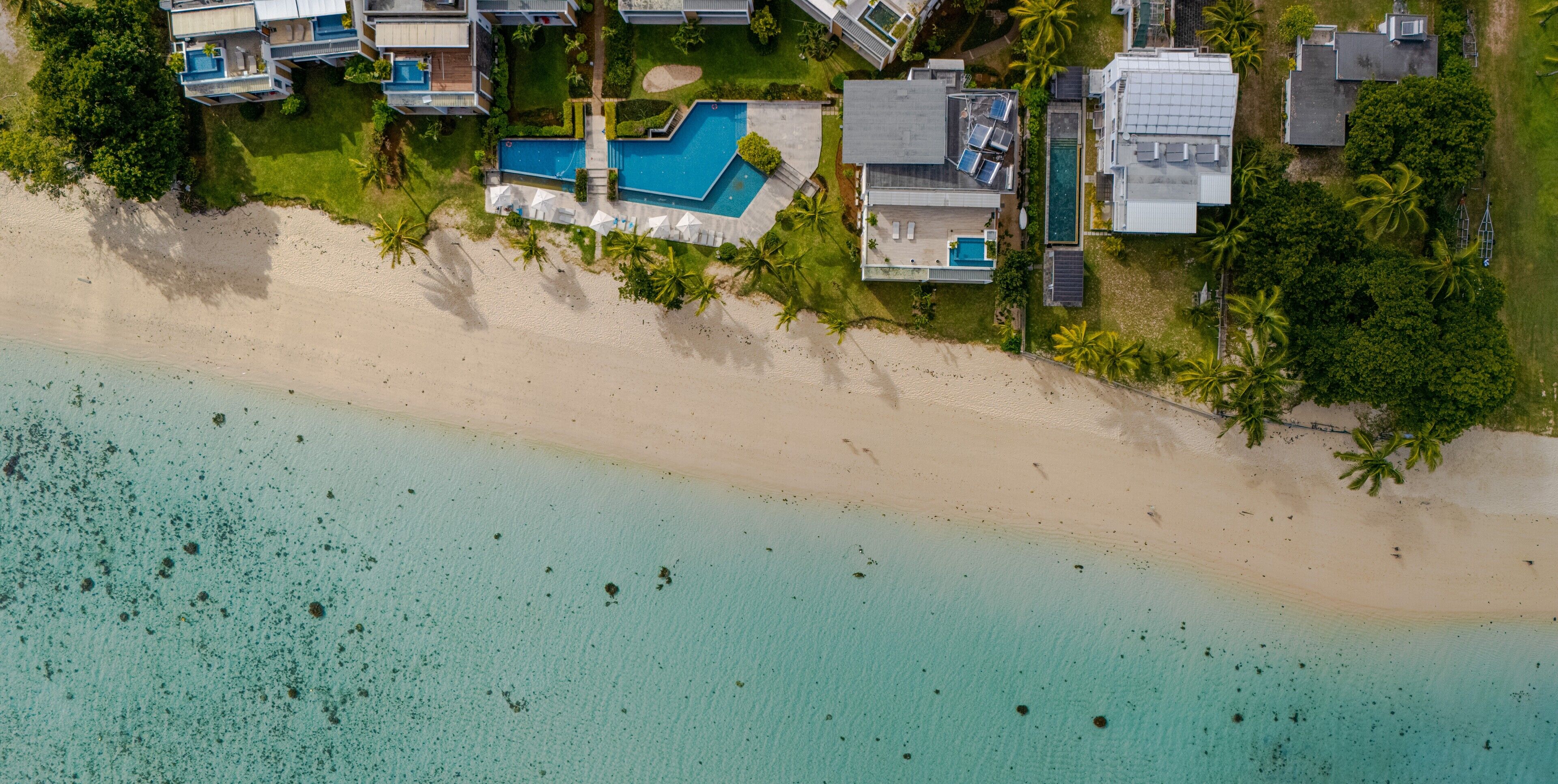 Vista aérea de una propiedad costera con piscina, varias edificaciones y una playa.