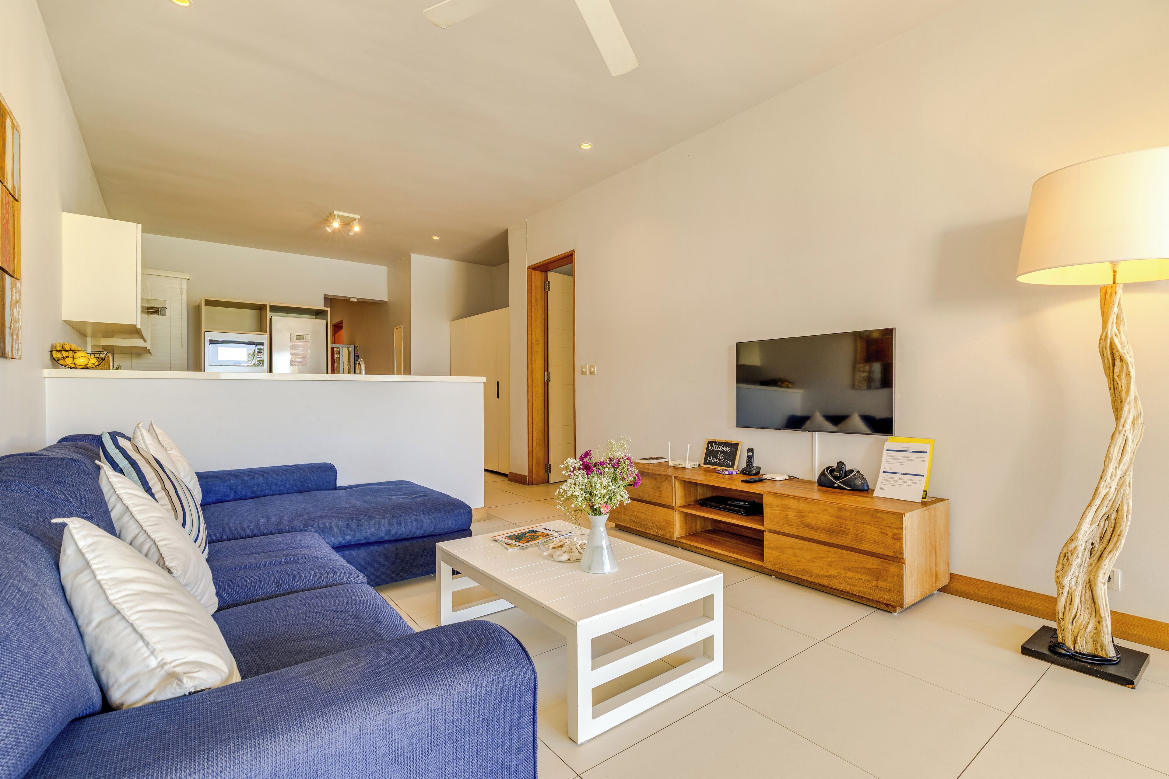 A modern living room with a blue sofa, a white coffee table, a wooden entertainment unit, and a flat-screen TV.