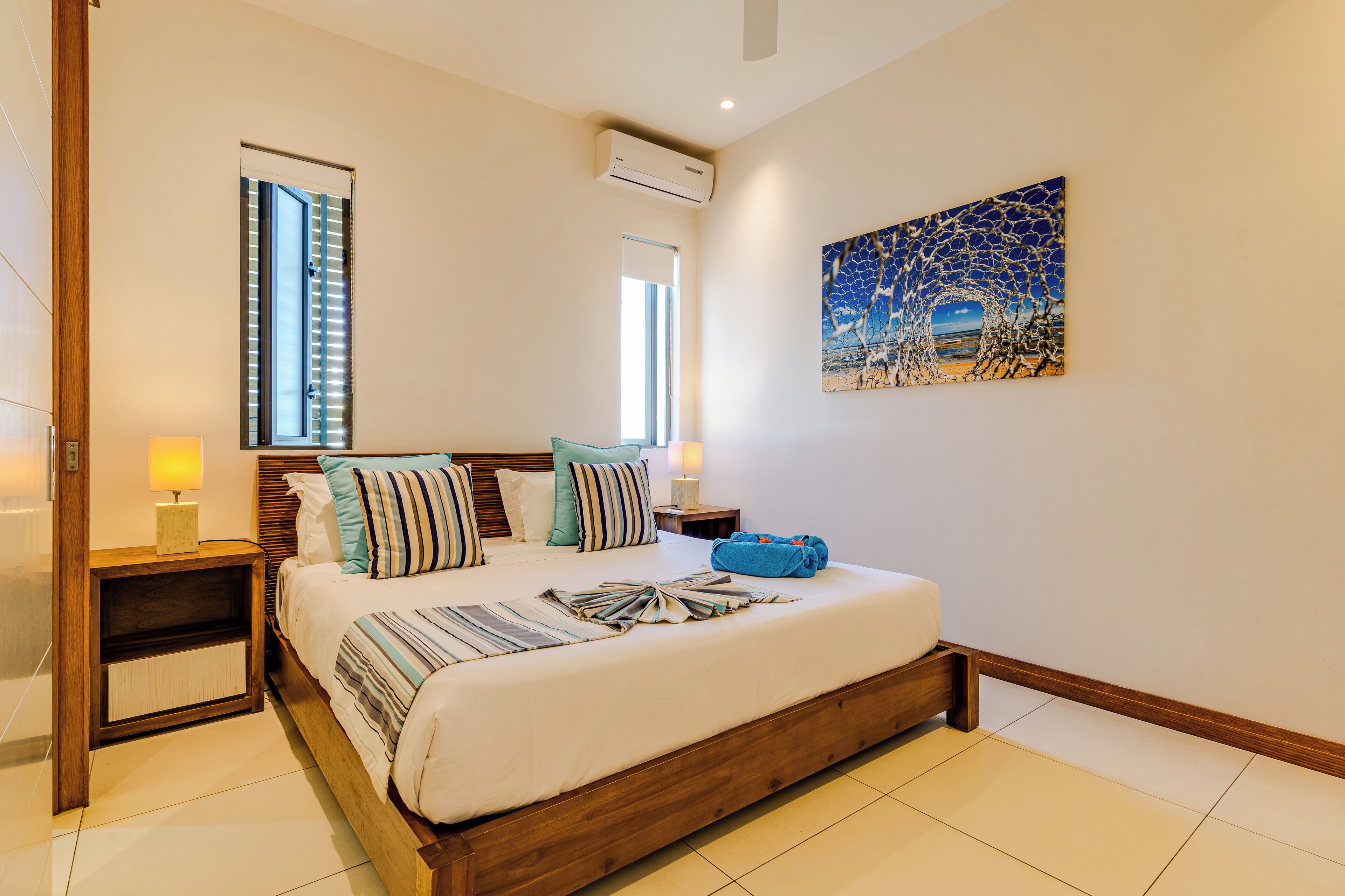 A bedroom with a large bed, two bedside tables, a window, and a wall-mounted air conditioner.
