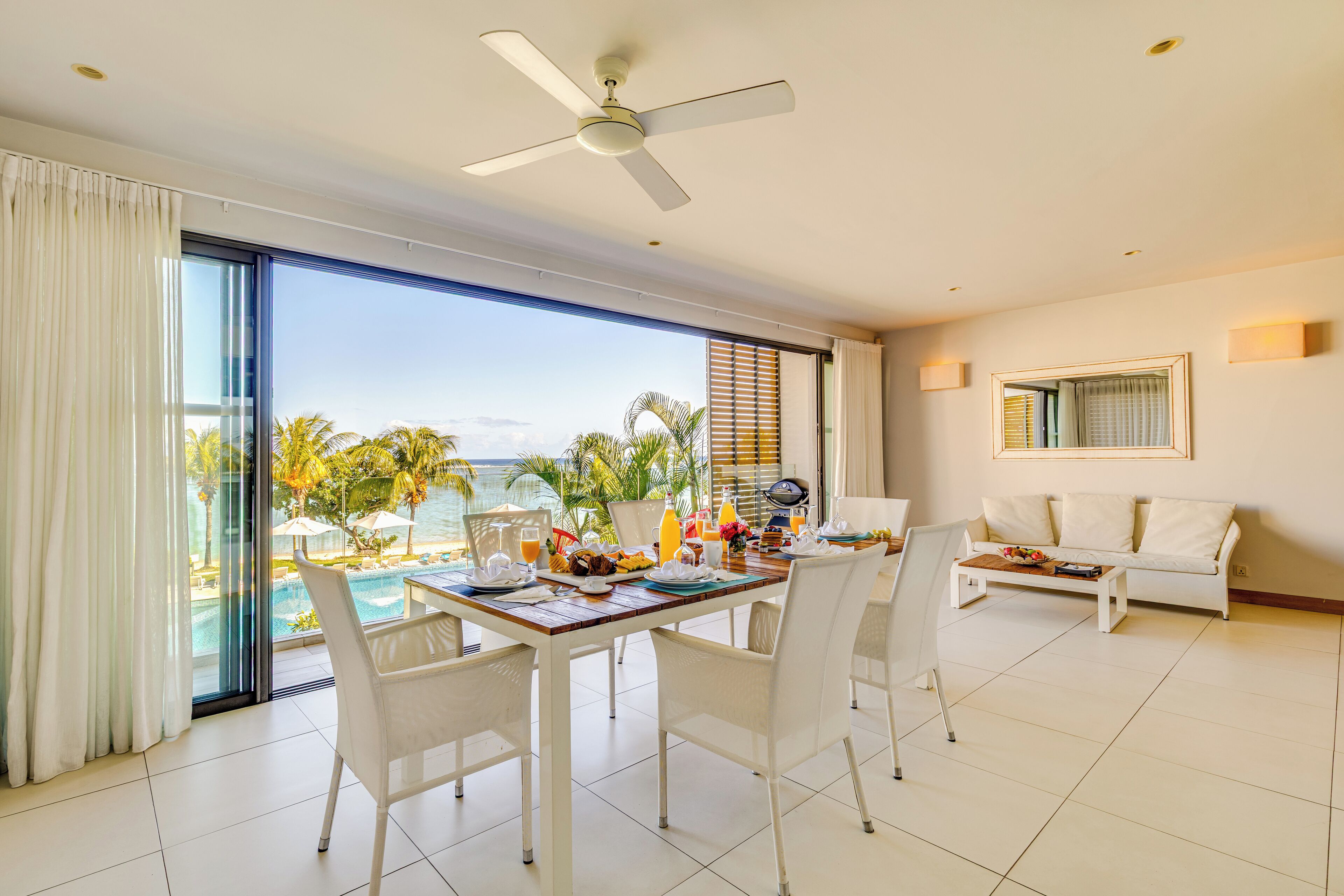 A modern dining area with a table set for breakfast, a white sofa, and a view of the ocean.
