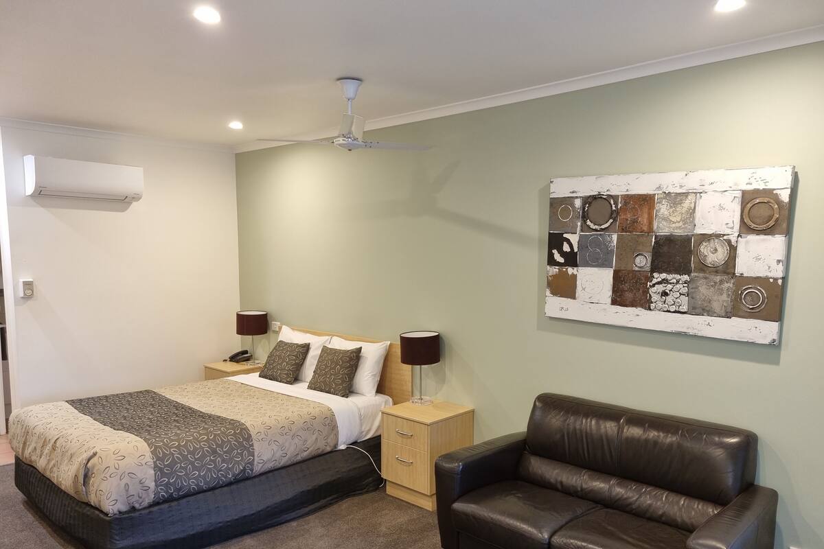 A bedroom with a bed, bedside tables, a leather sofa, a ceiling fan, and a wall art piece.