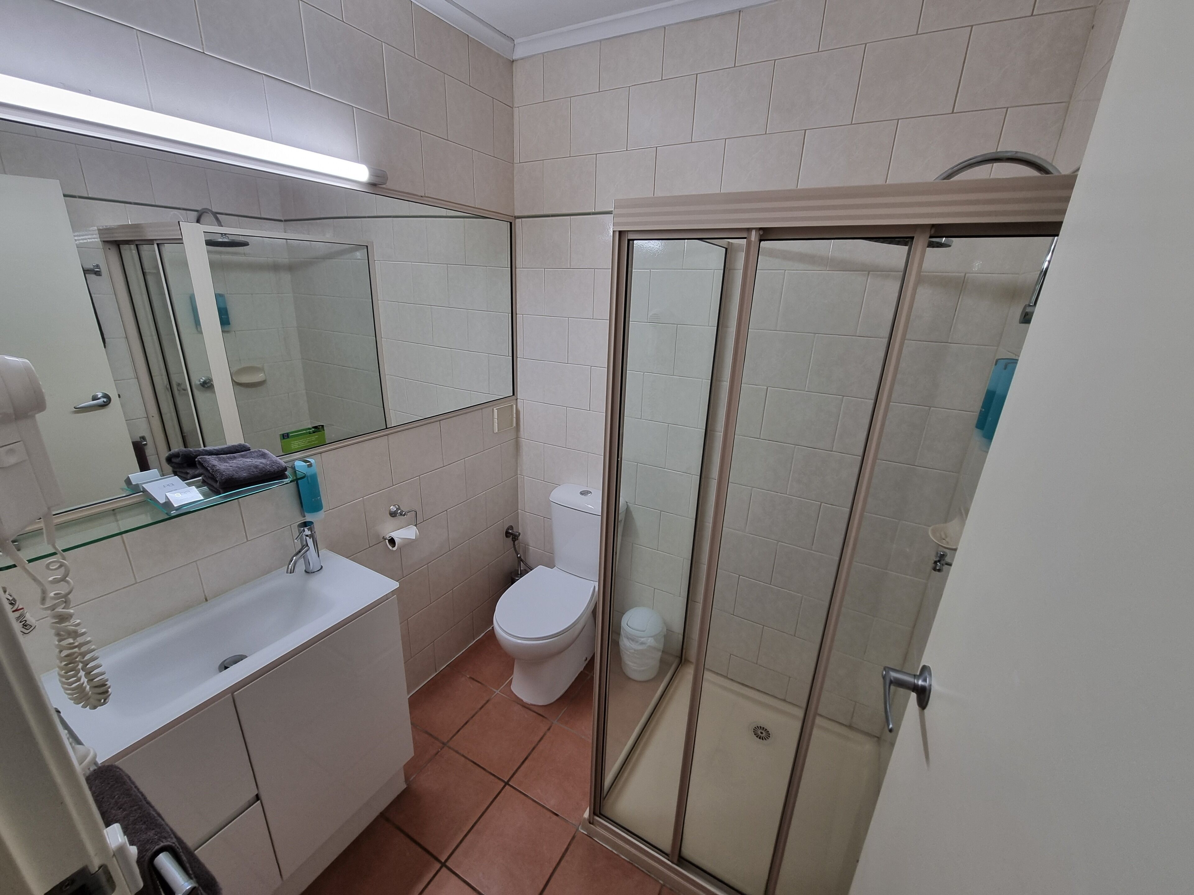 Un baño con cabina de ducha de vidrio, inodoro, lavamanos con espejo y un perchero para toallas.