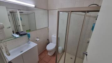 Un baño con cabina de ducha de vidrio, inodoro, lavamanos con espejo y un perchero para toallas.