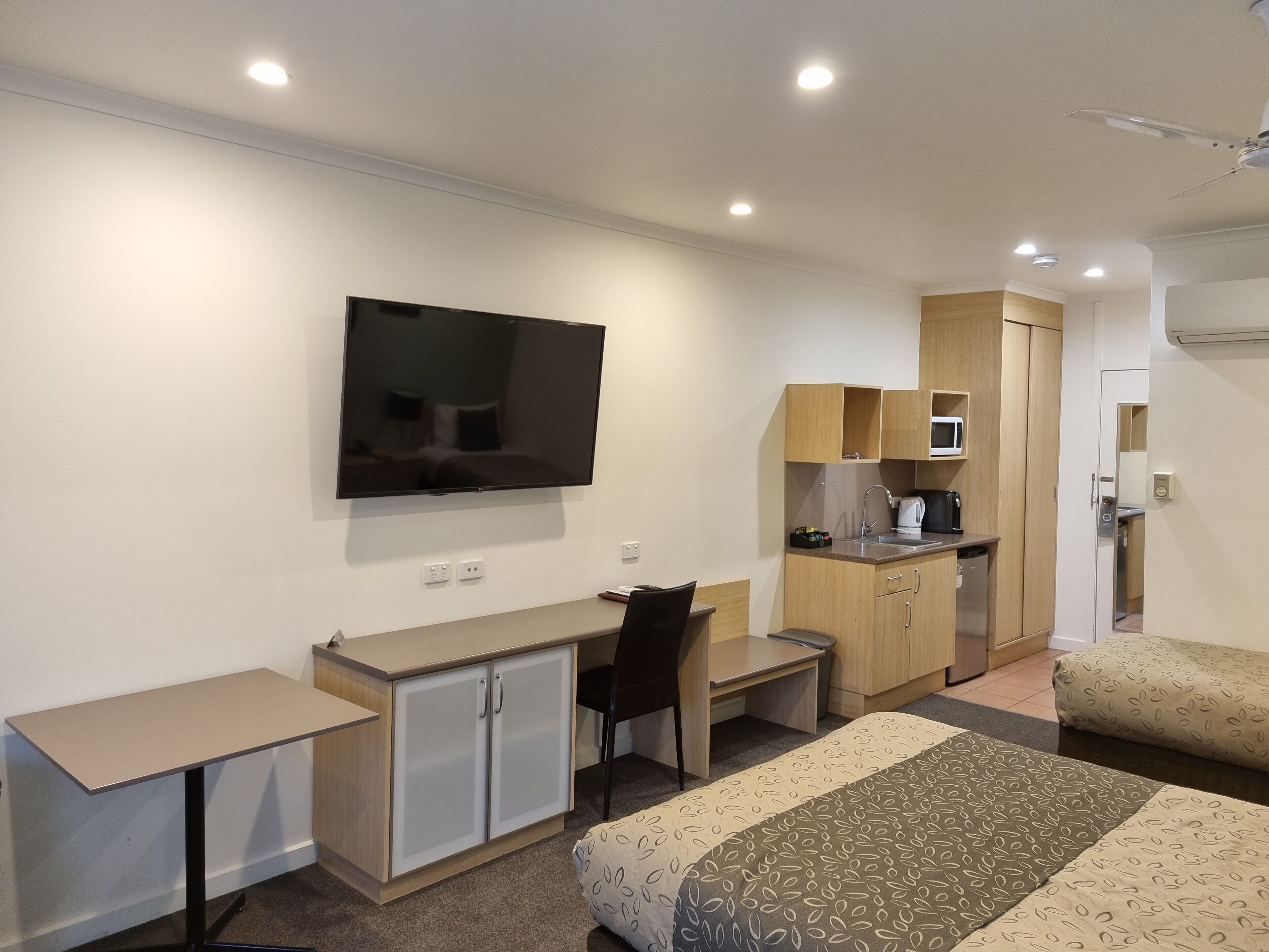 A hotel room with a bed, a desk, a chair, a television, a kitchenette, and a bathroom.
