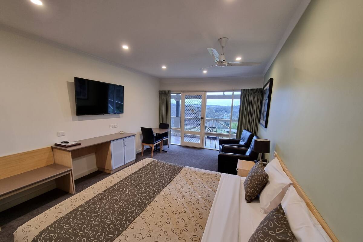 A hotel room with a bed, desk, chair, TV, and a balcony with a view.
