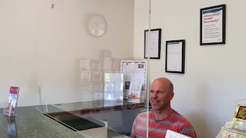Un mostrador de recepción con una separadora de vidrio, un reloj y carteles informativos en la pared.
