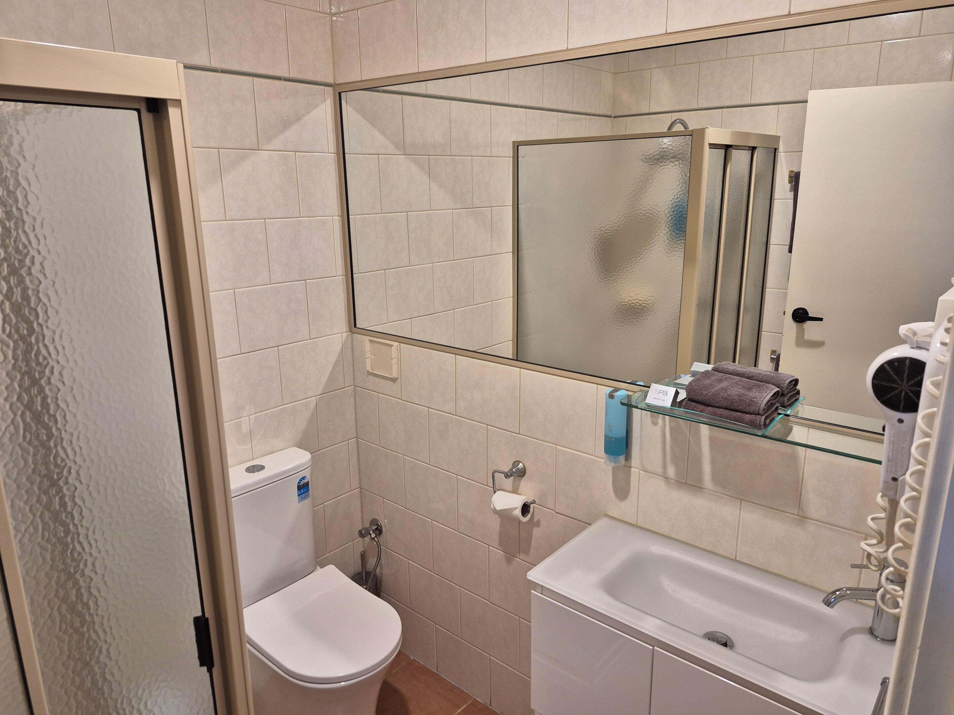 Un baño con inodoro, lavabo y repisa de vidrio con toallas.