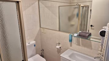 Un baño con inodoro, lavabo y repisa de vidrio con toallas.