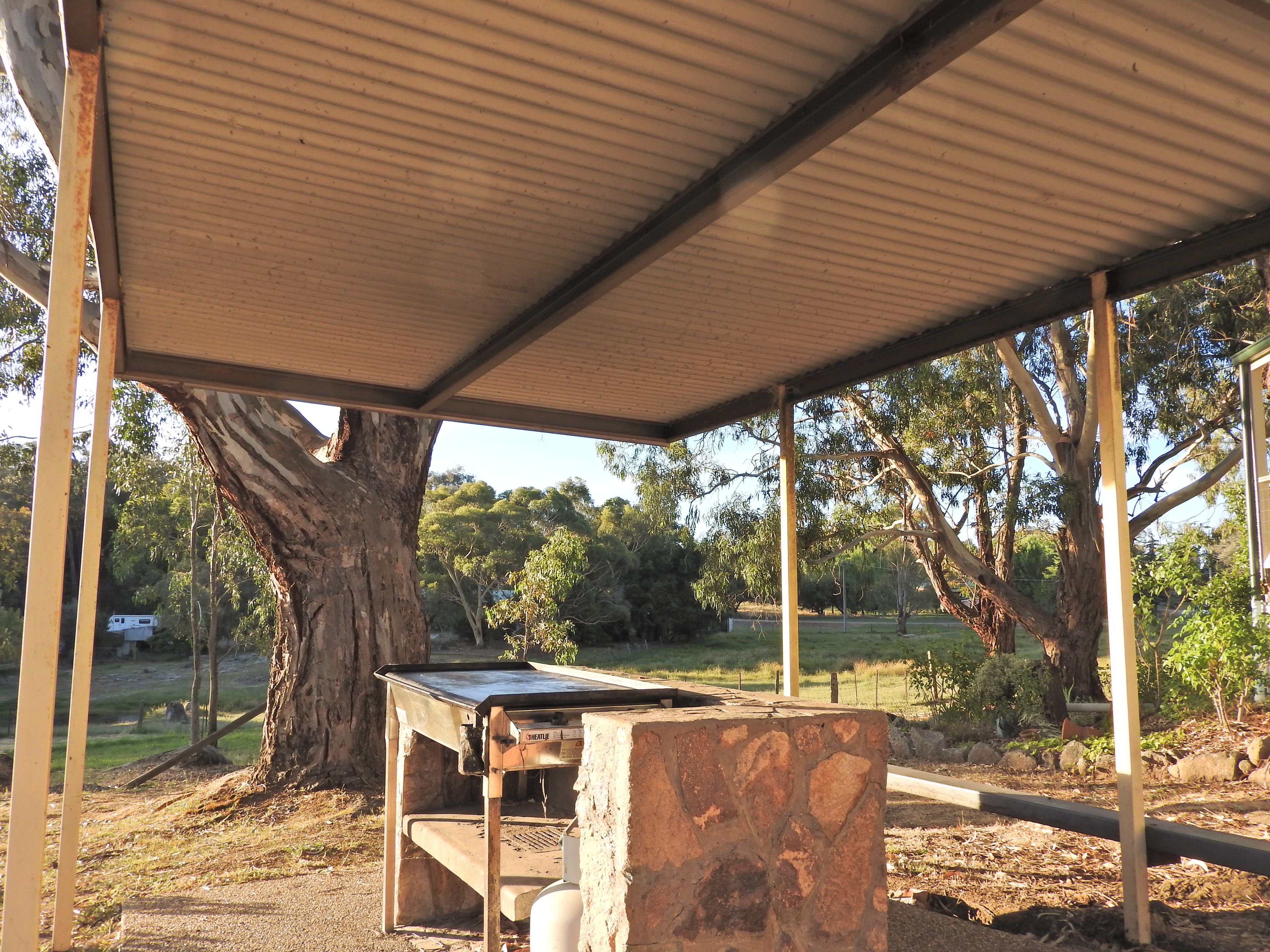 An outdoor covered area with a table and stone block, surrounded by trees and a grassy field.