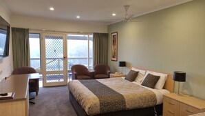 A hotel room with a bed, desk, chairs, a desk lamp, a bedside table, a telephone, and a view through the glass doors. - Golden Heritage Accommodation (Beechworth)