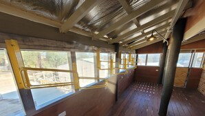 A train carriage interior with wooden flooring, metal handrails, and large windows. - Golden Heritage Accommodation (Beechworth)