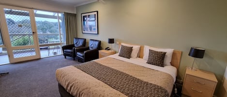Habitación de hotel con una cama grande, dos mesitas de noche, un ventilador de techo y vistas a través de un gran ventanal corredizo.
