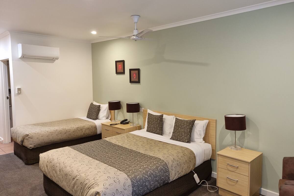 A hotel room with two beds, bedside lamps, a nightstand, a lamp on the floor, and an air conditioning unit.