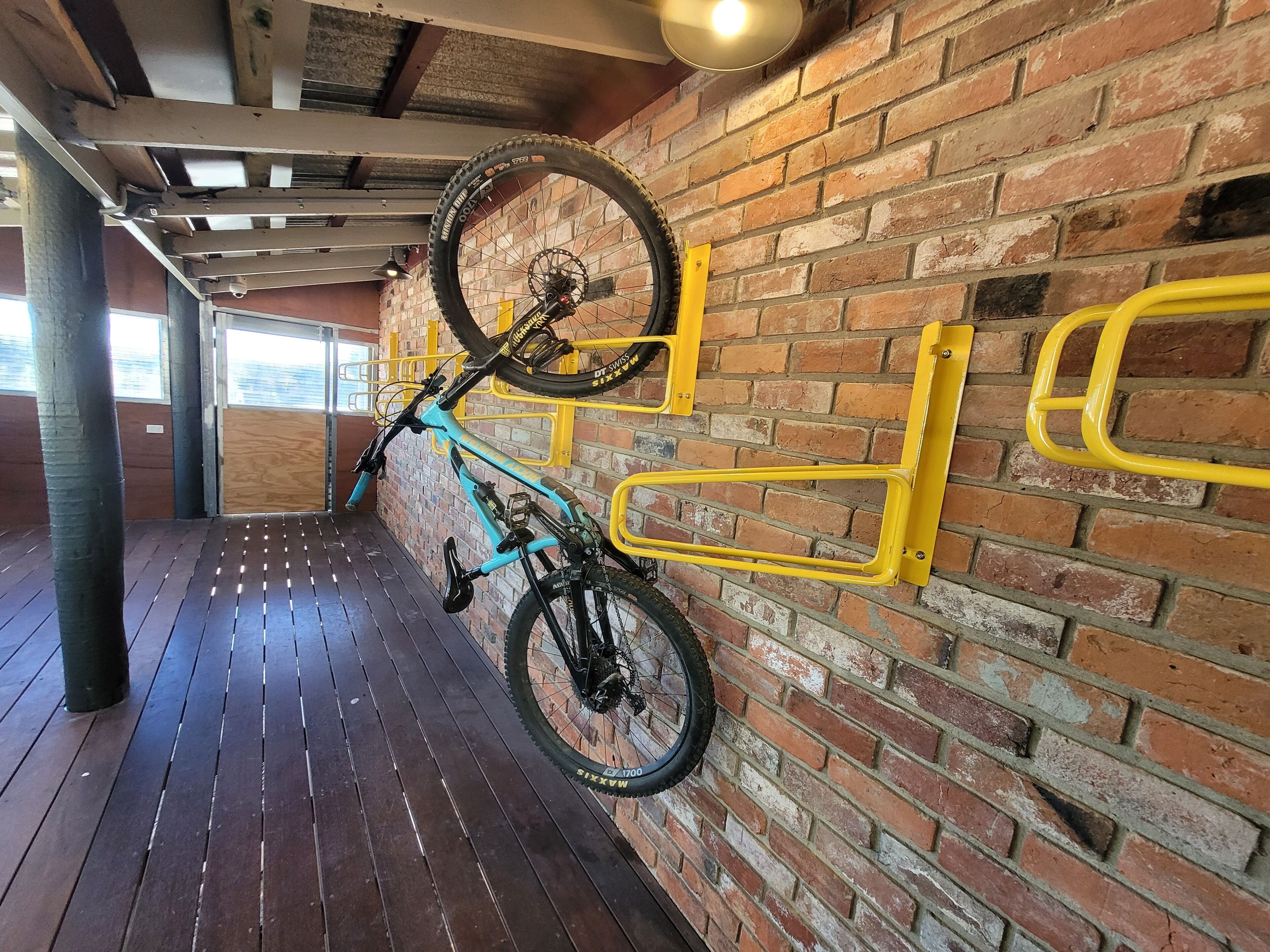 A room with a brick wall, wooden flooring, and a bike mounted on a yellow rack.