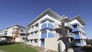 A modern multi-story residential building with balconies, large windows, and a flat roof design.