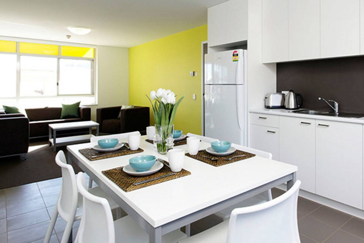 A modern kitchen with white cabinets, a built-in refrigerator, and a dining area with a white table and chairs.