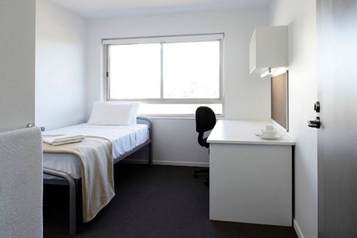 A small, clean room with a bed, a desk, and a window.