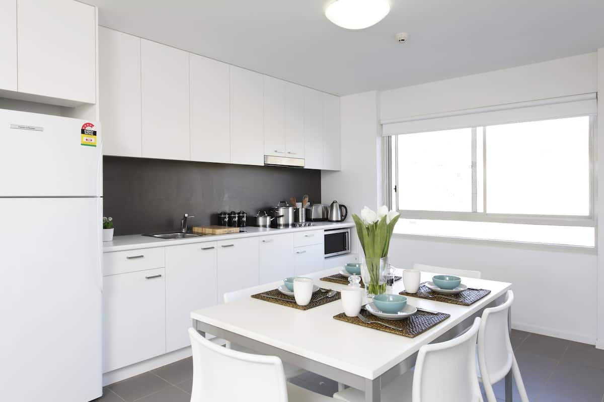 A modern kitchen with white cabinetry, a dining table set with blue and white tableware, and a window providing natural light.