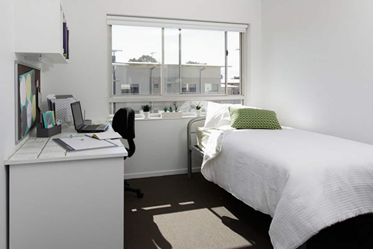 A small, clean room with a desk, chair, bed, and window.