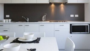 A modern kitchen with white cabinetry, a black backsplash, and a built-in microwave.