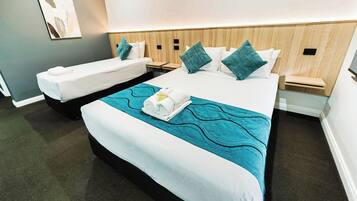 A hotel room with two single beds, a larger bed, and a small table between them.