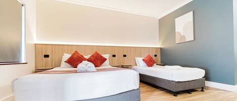 Habitación de hotel moderna con dos camas, cabecera de madera y una pared azul decorativa.