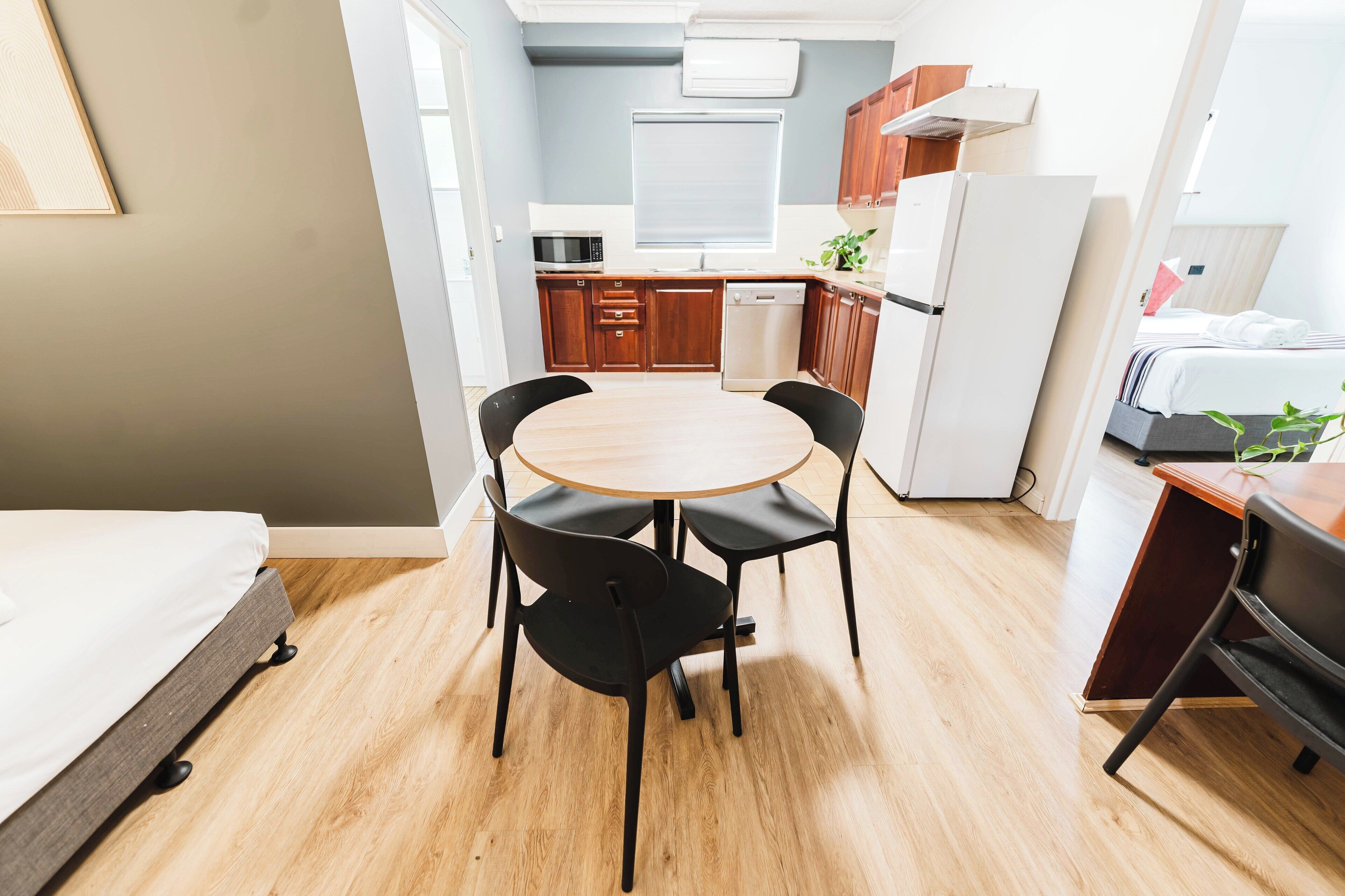A compact hotel room with a bed, a small dining table with chairs, a kitchenette, and a bathroom.