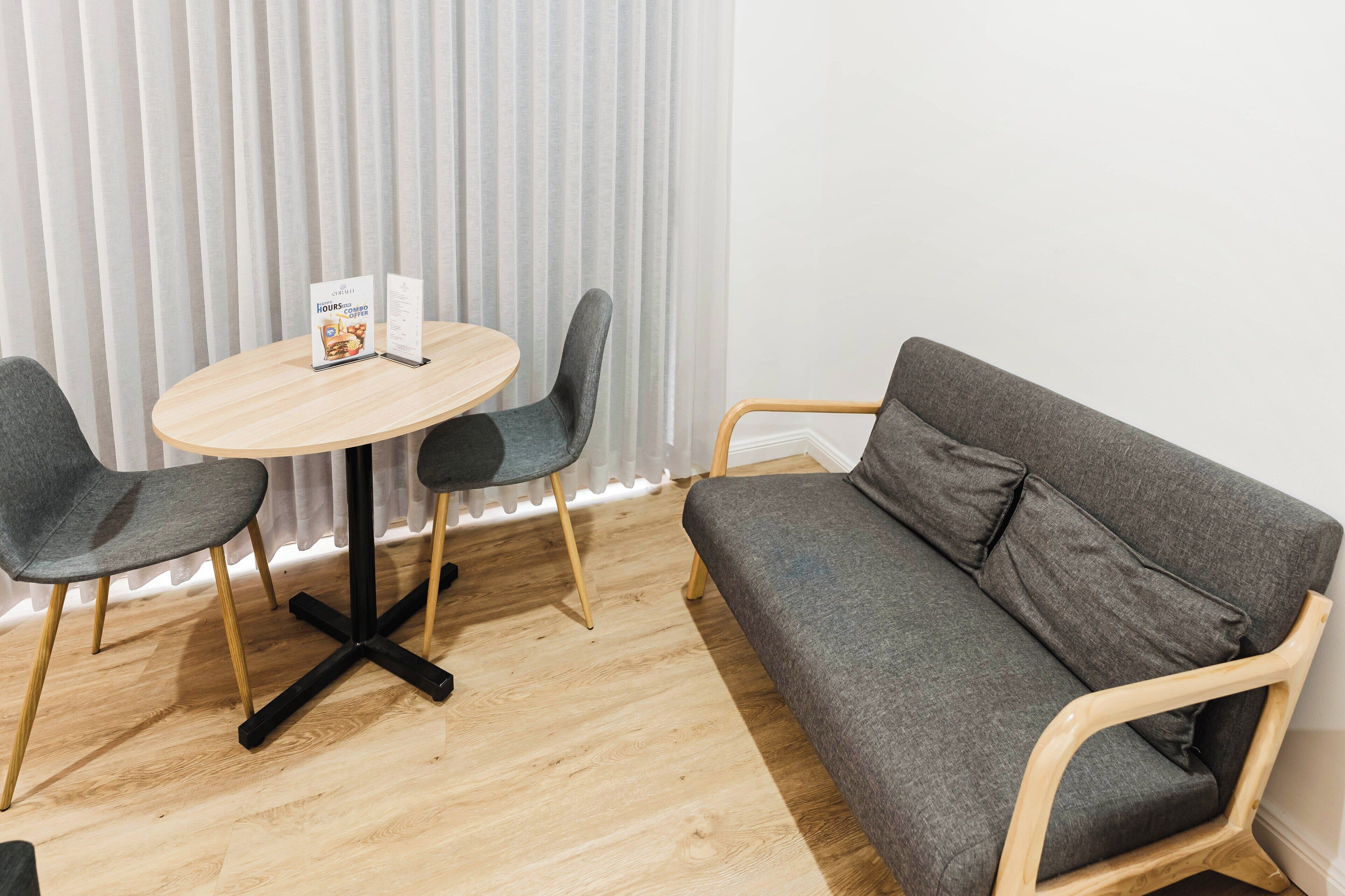 A modern room with a round wooden table, two grey chairs, and a grey sofa.