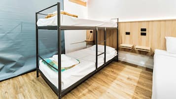 Habitación con literas, suelo de madera, un escritorio pequeño de madera y una cama blanca.
