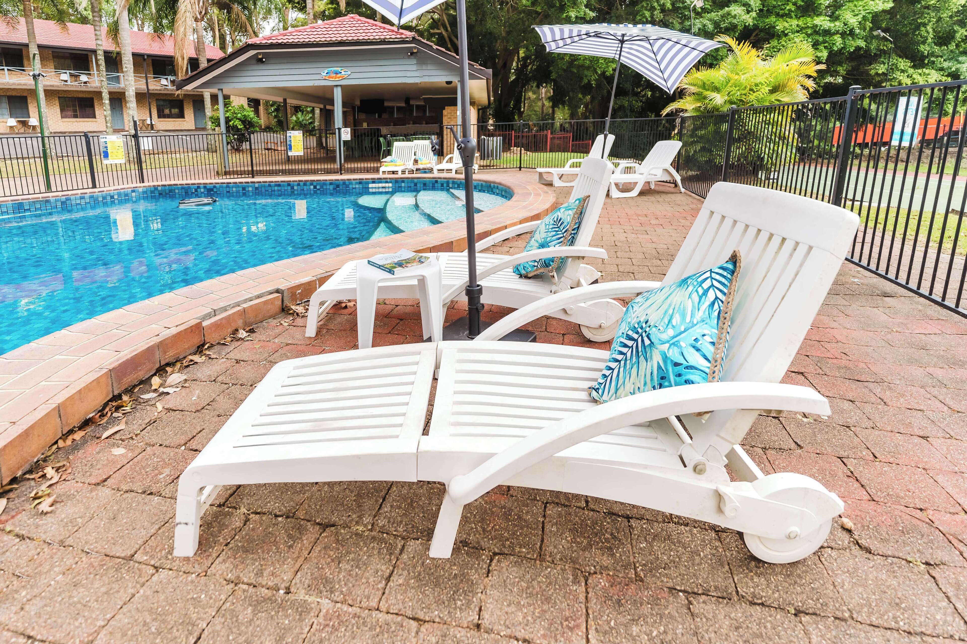 Un espace aménagé au bord de la piscine, avec des chaises longues blanches, une piscine et un coin salon abrité.