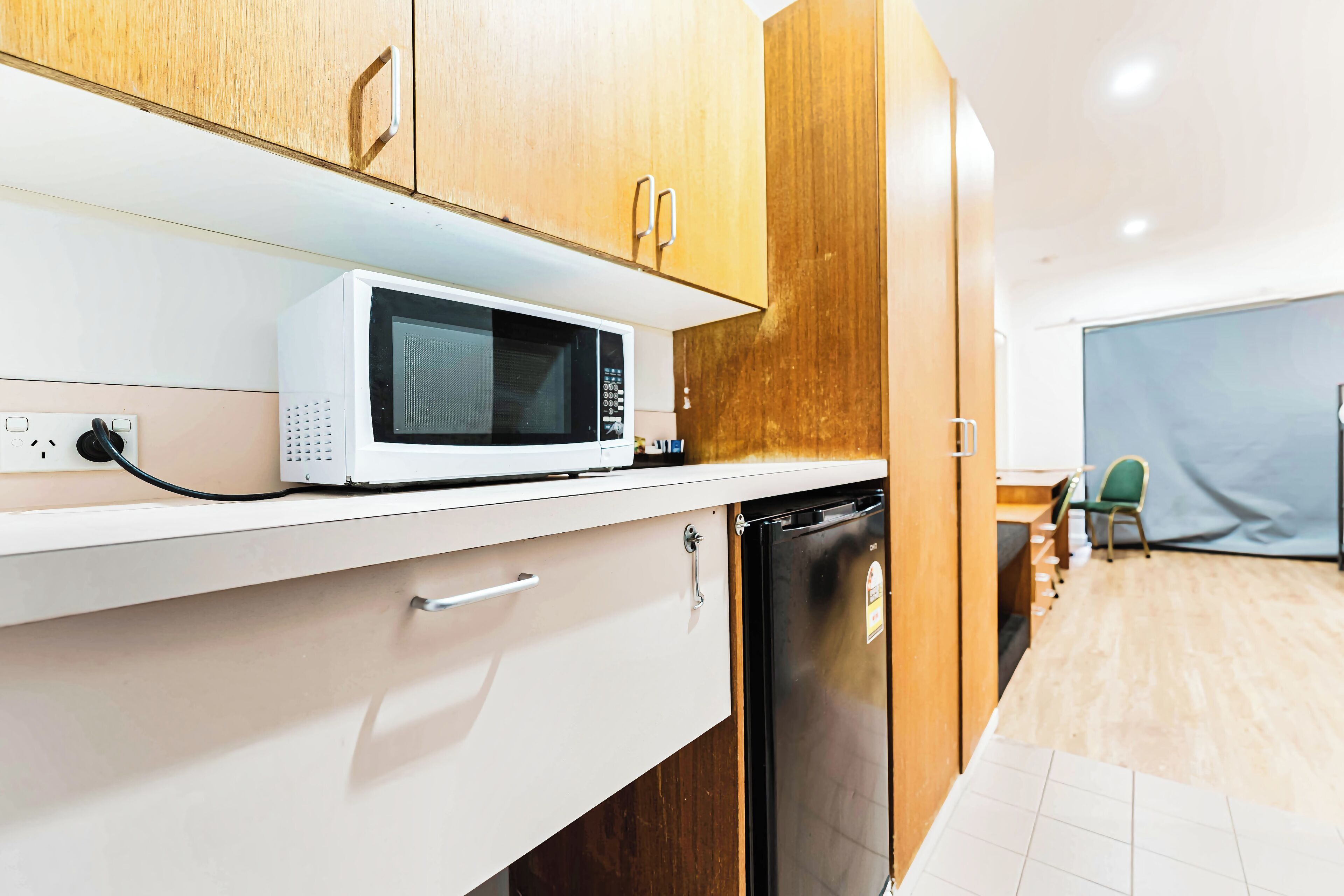 A kitchen with wooden cabinets, a white countertop, a microwave, a dishwasher, and a small table with a chair.
