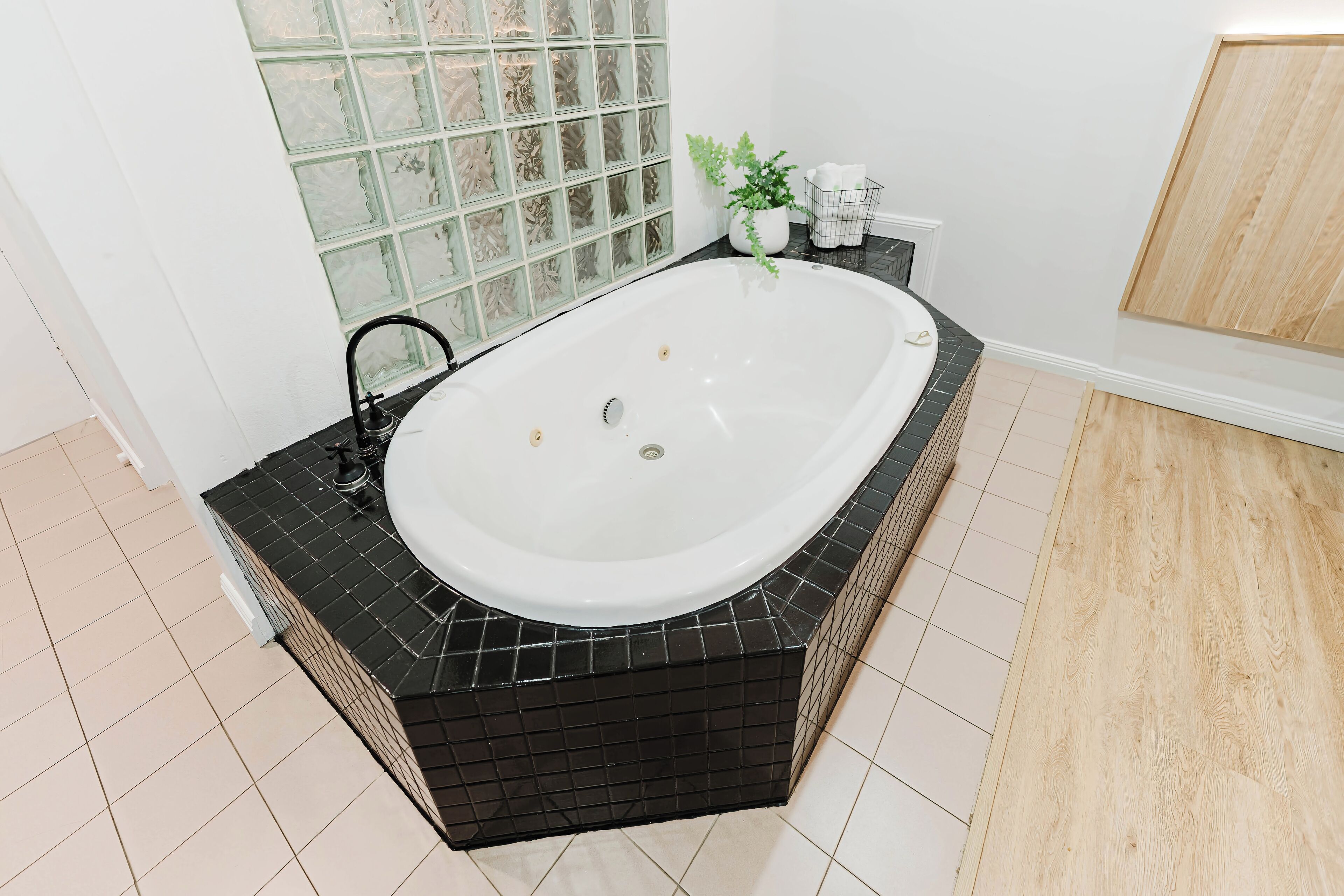 A modern bathroom with a freestanding bathtub, black tiled surround, a glass shower enclosure, and a wooden floor.