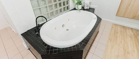A modern bathroom with a freestanding bathtub, black tiled surround, a glass shower enclosure, and a wooden floor.