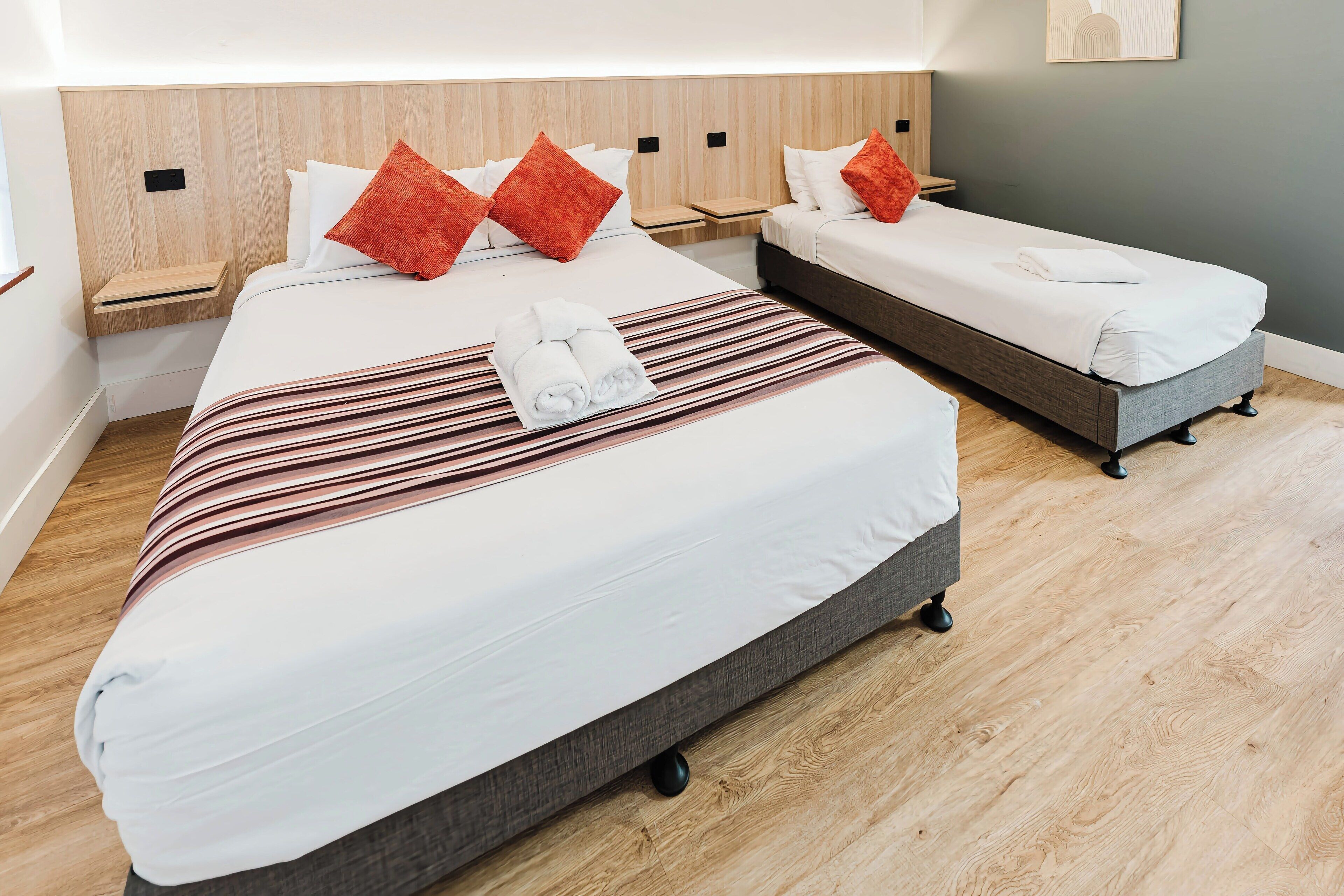 A hotel room with two beds, a striped blanket, and red pillows.