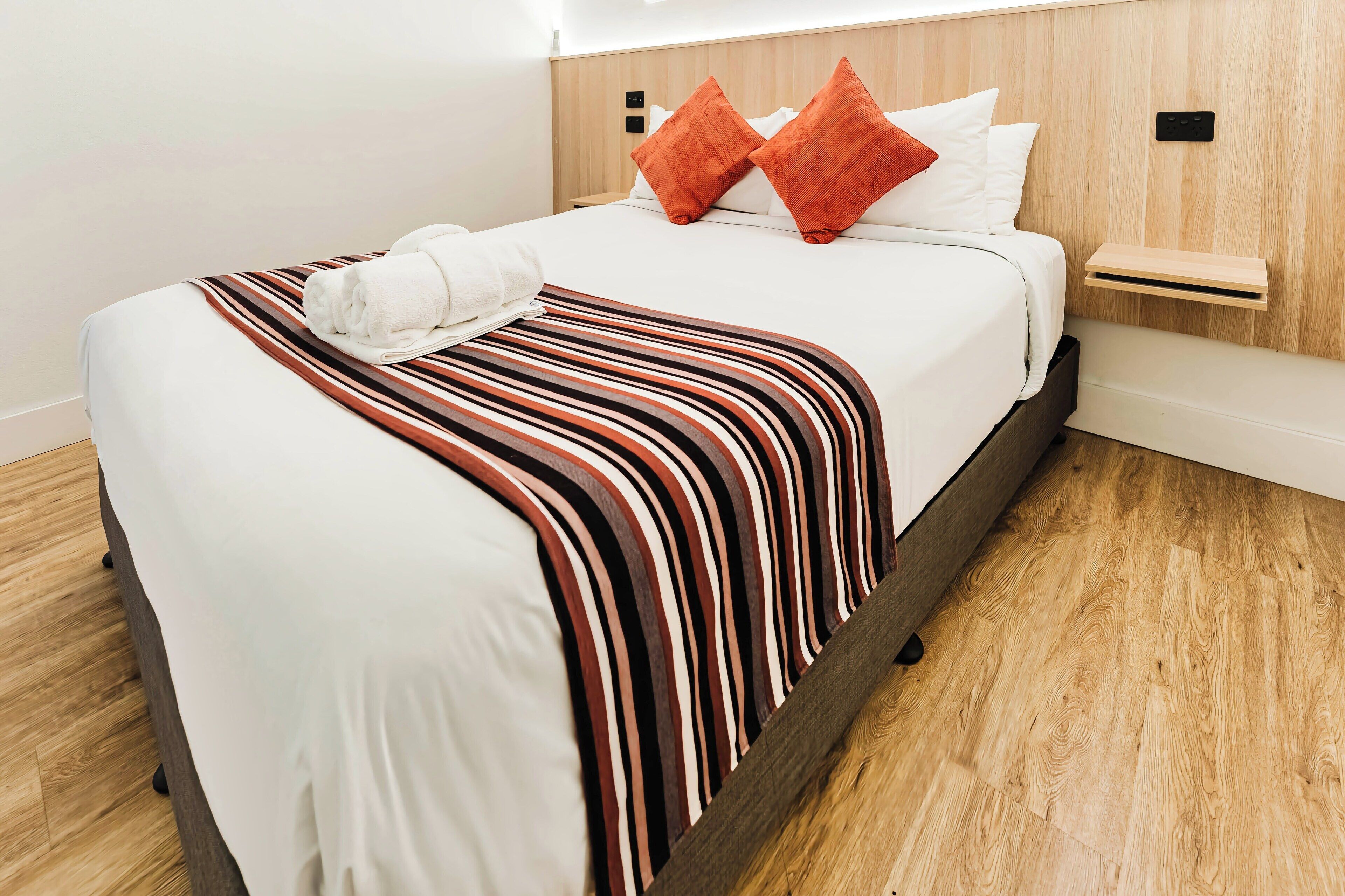 A neatly made bed with a striped blanket, two pillows, and a folded towel on the side.