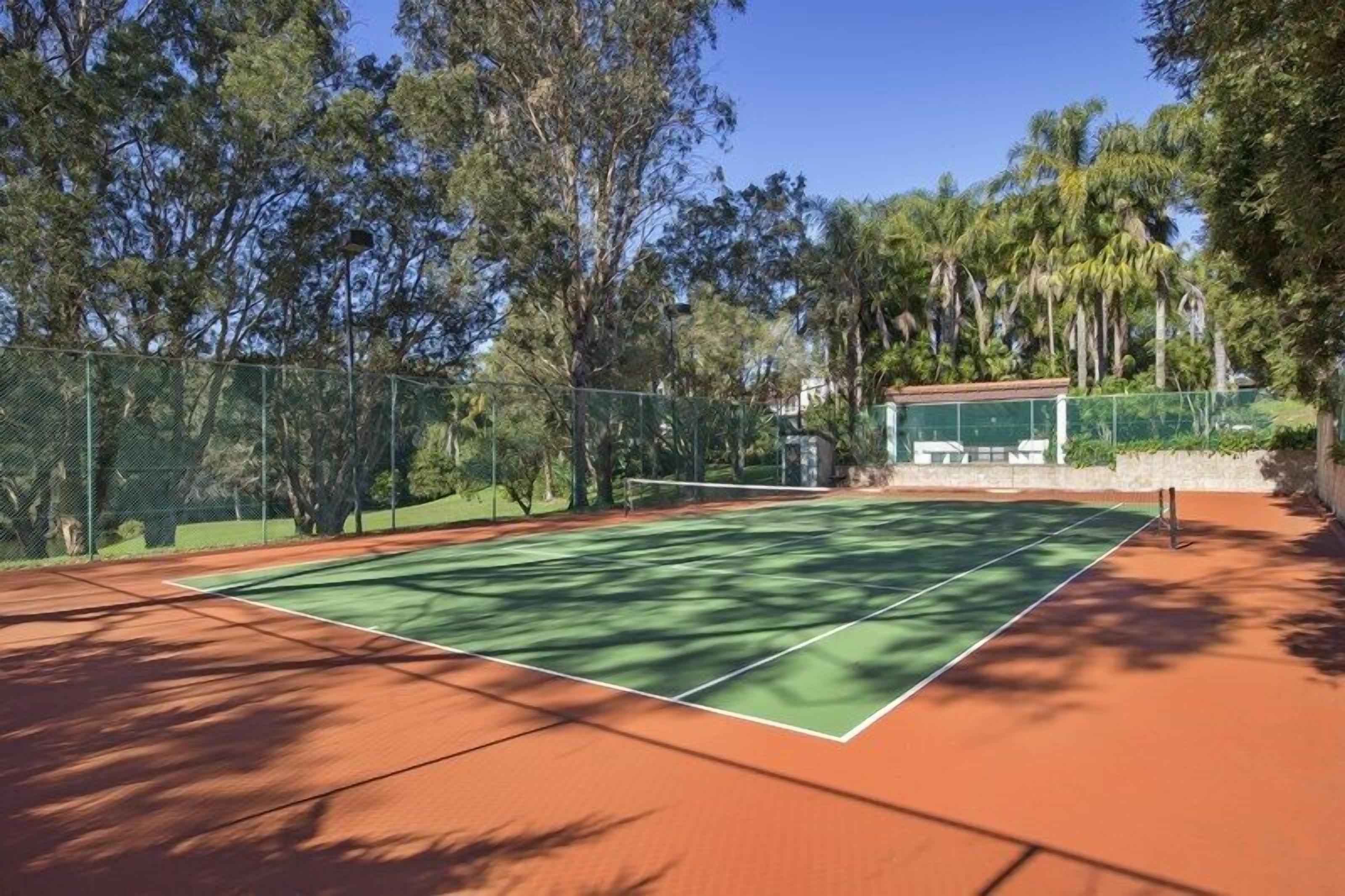An outdoor tennis court surrounded by trees and a fence.