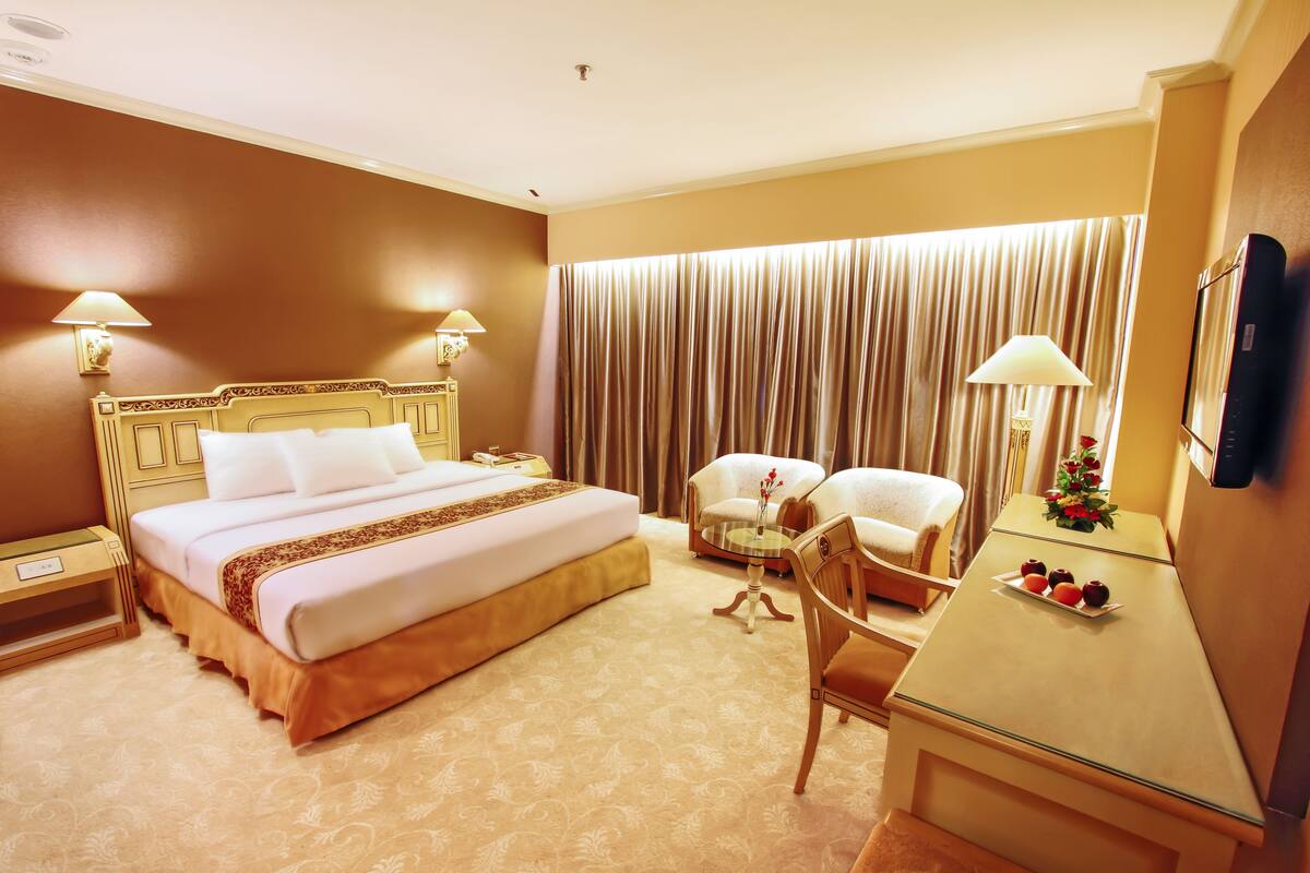 A hotel room with a large bed, two chairs, a small table, and a TV on a cabinet.