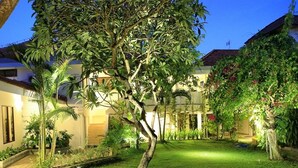 A well-maintained garden with a variety of plants and a central tree, surrounded by a building with a tiled roof and a balcony. - Patrisia Hotel Bali (Denpasar)