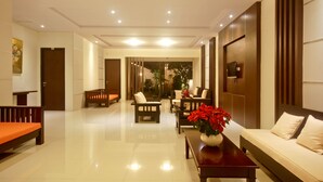 A spacious lobby with a polished floor, a sofa, a coffee table with a vase of flowers, and a wooden bench. - Patrisia Hotel Bali (Denpasar)
