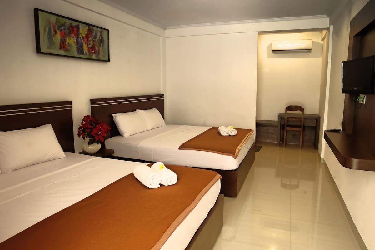 Quarto de hotel com duas camas, uma televisão, uma mesinha e um quadro na parede.