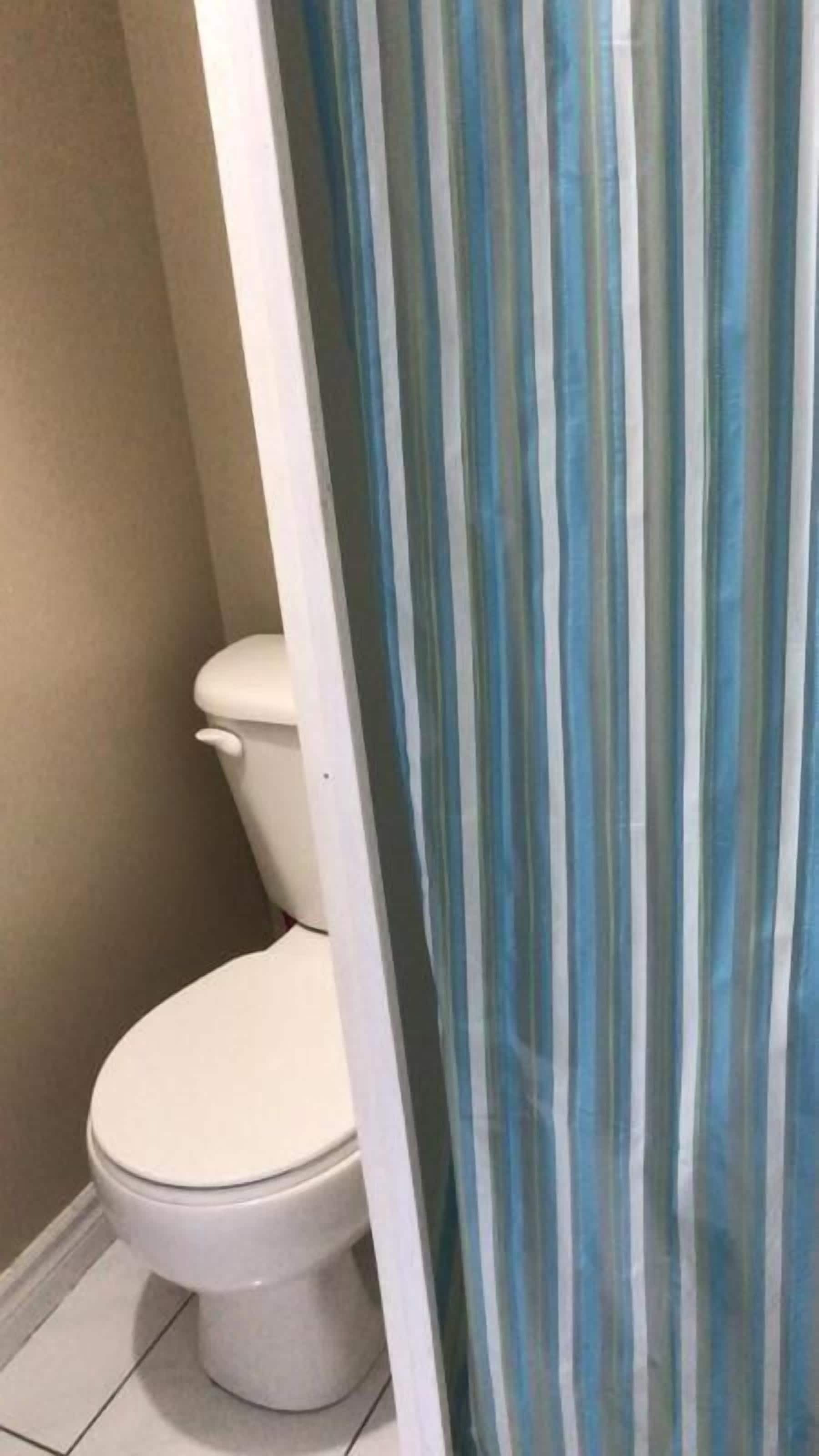 A bathroom with a toilet, a striped shower curtain, and a tiled floor.