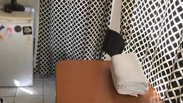 A small room with a patterned curtain, a fan, a refrigerator, and a chair with a towel.