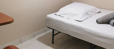 Una habitación pequeña con una cama individual, una silla y una mesa.