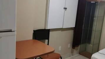A small, clean room with a white wardrobe, a table with two chairs, a bed, and a shower area.