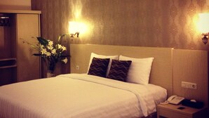 A hotel room with a bed, bedside table, and a nightstand with a phone and a lamp. - Ramayana Hotel (Makassar)